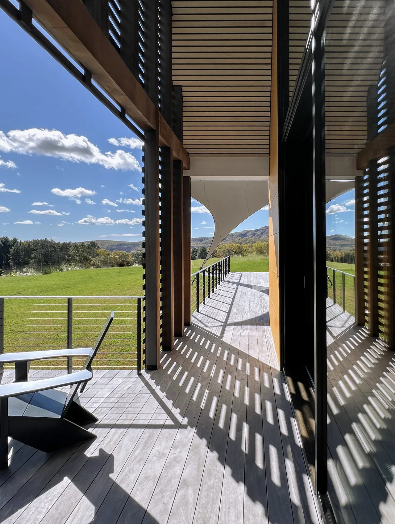 Deck with wood slat ceiling and metal railing features a fabric canopy and views over a grassy field and hills.