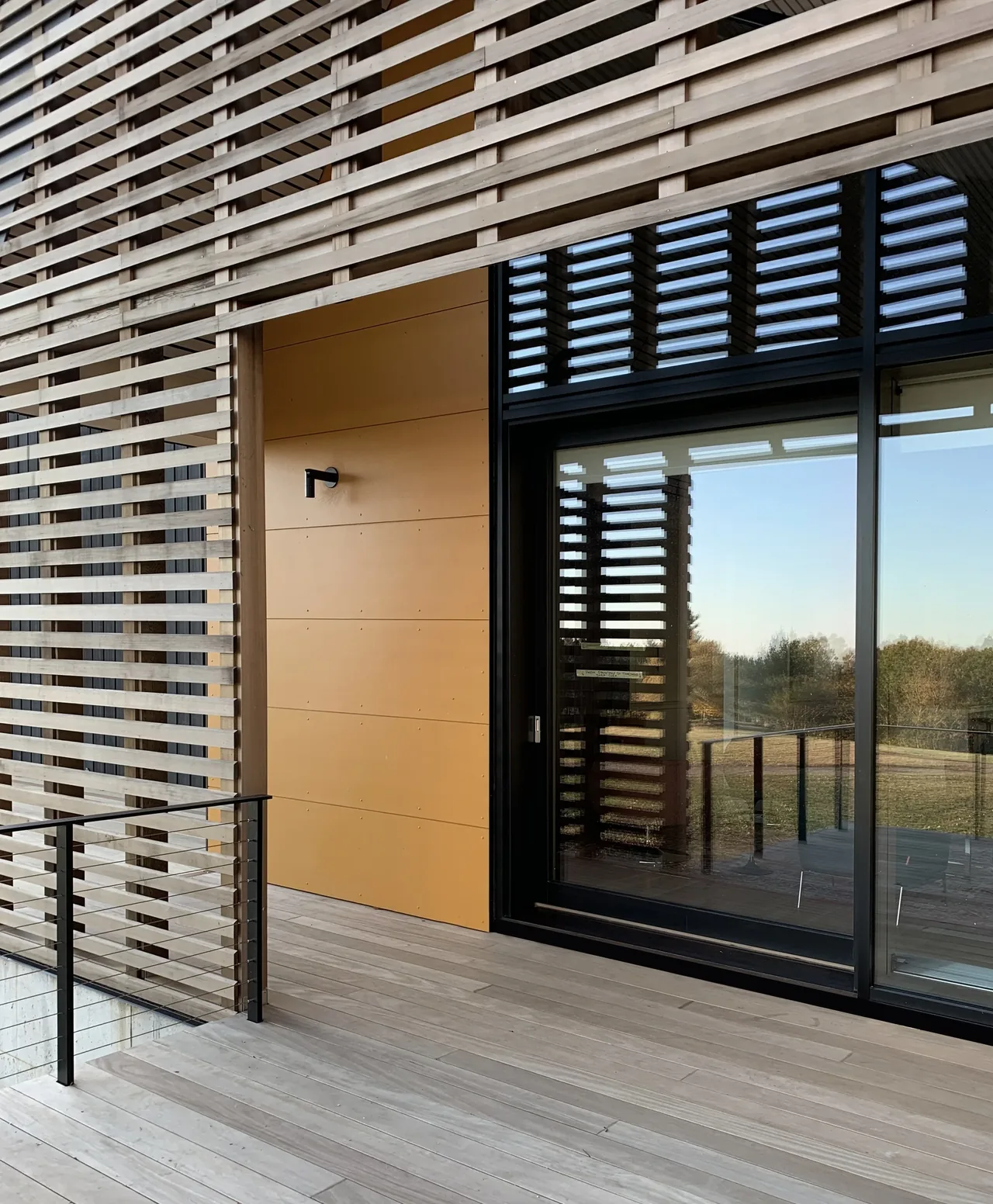 Deck area with horizontal wood lattice screen, black sliding glass doors, and yellow panel on an exterior wall.