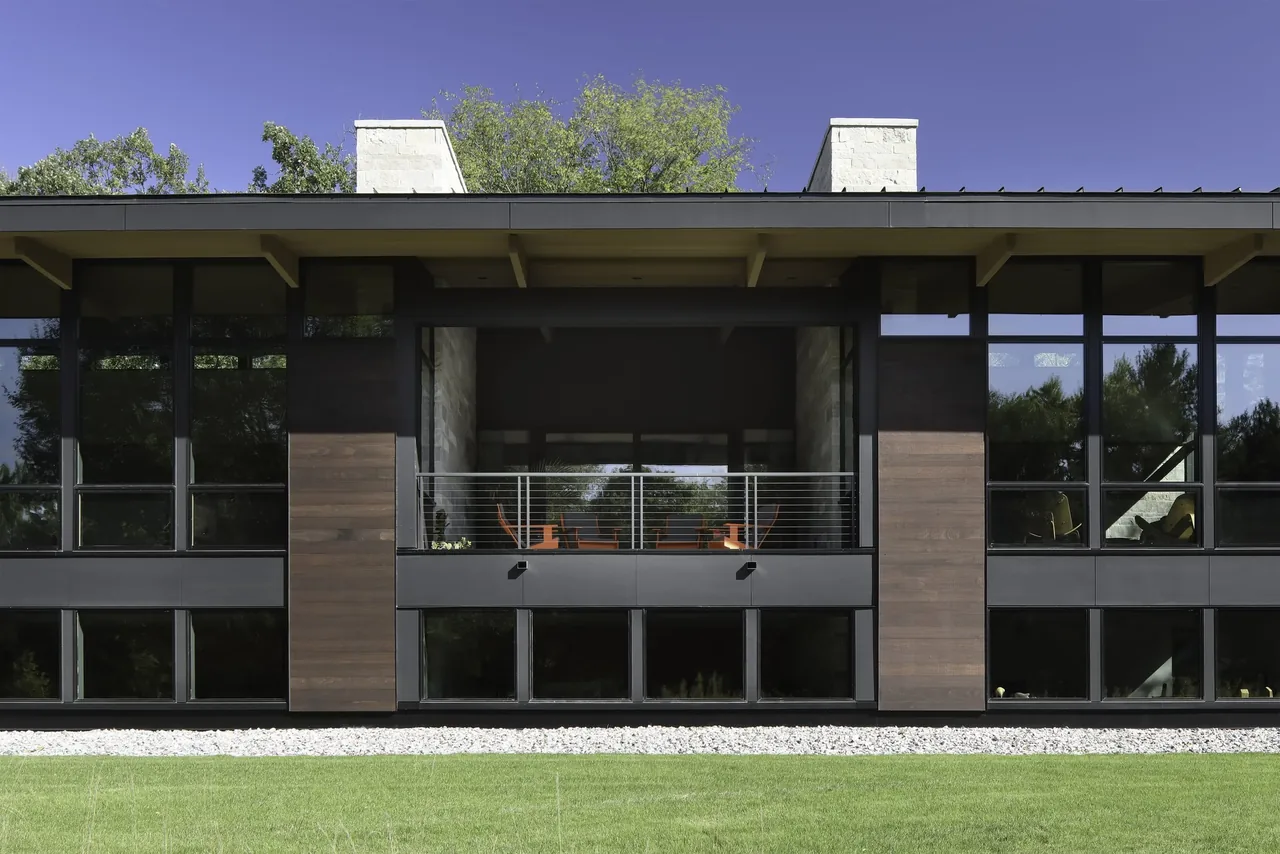 Front exterior of the Art & Music House featuring large black-framed windows, wood siding panels, and a recessed balcony with cable railing.