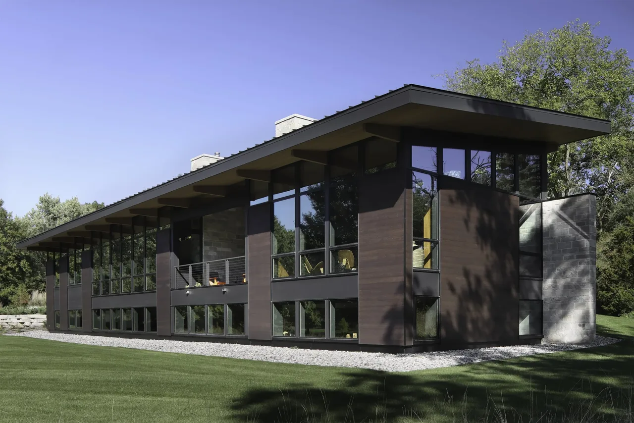 Modern flat-roofed house with dark wood siding, black window frames, and extensive floor-to-ceiling glazing.