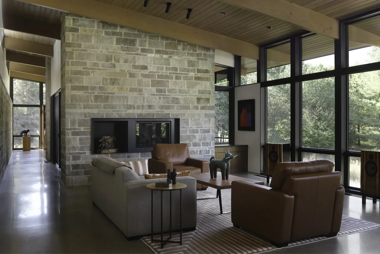 Living room of Art & Music House with large black-framed windows and a stone fireplace wall.
