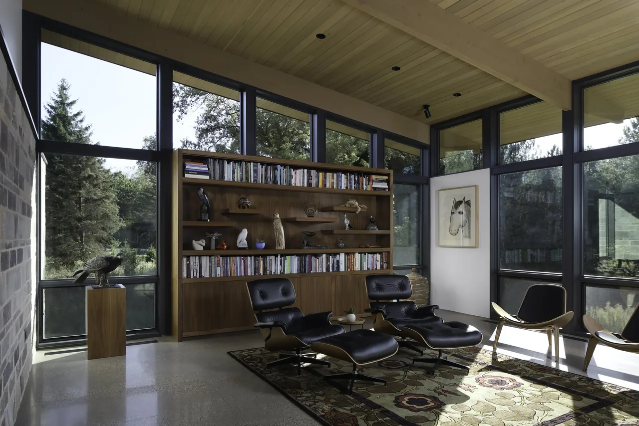 Living room with extensive floor-to-ceiling glazing, black window frames, wooden ceiling, and mid-century modern furniture.