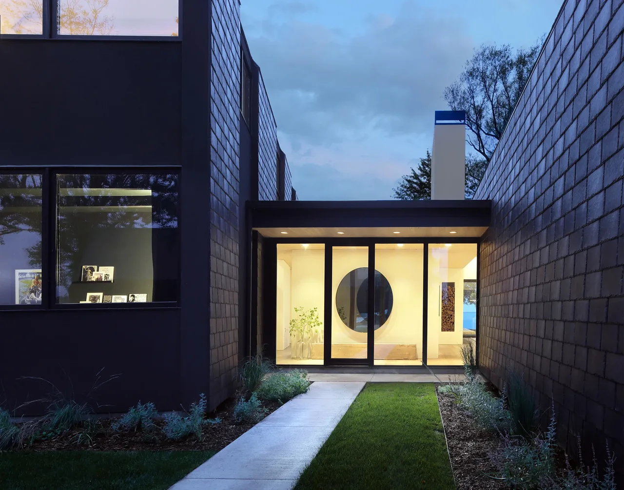 Entrance view of Woven House featuring a matte black facade and tall windows with a glass entry bridge.