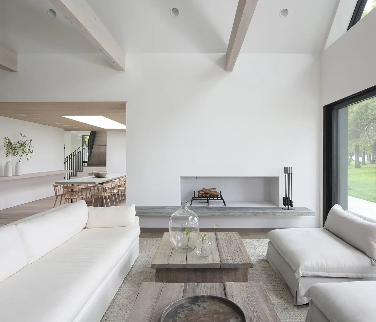 The Woven House living area features vaulted ceilings and a minimalist concrete fireplace with seating facing large windows.