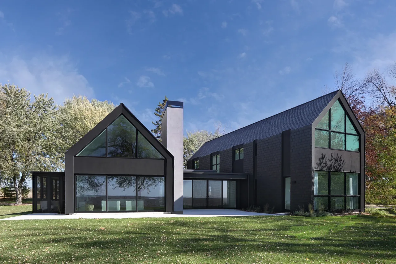 The Woven House features matte black facades with expansive glass gable windows and a connecting glass entry bridge.