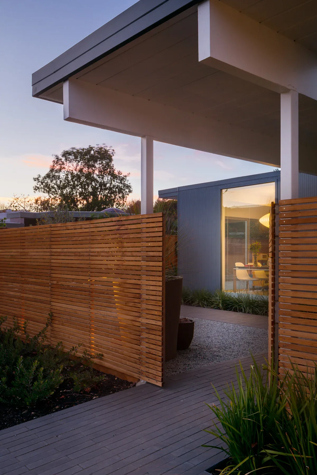 The Appleberry Drive Residence features a wood slat fence and gravel path leading to a modern home with large corner windows.