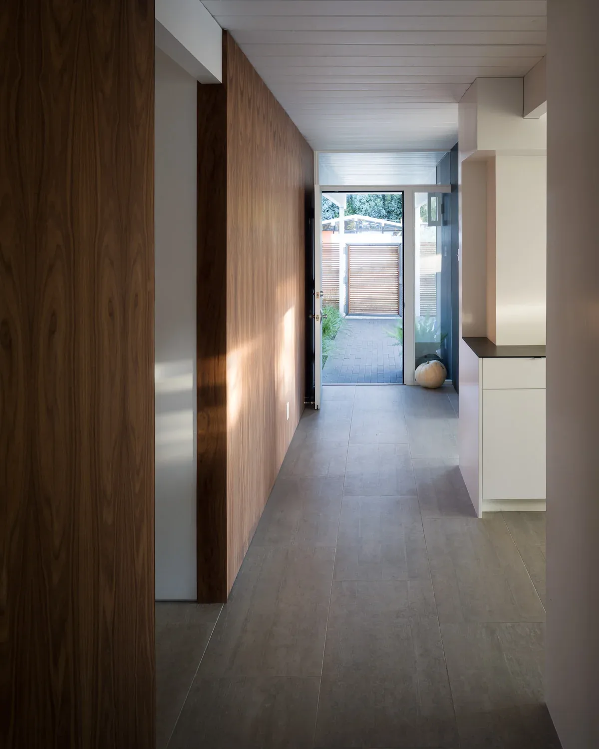 This interior hallway features wood panel walls and leads to a glass door opening to an outdoor space with a wooden slat gate.
