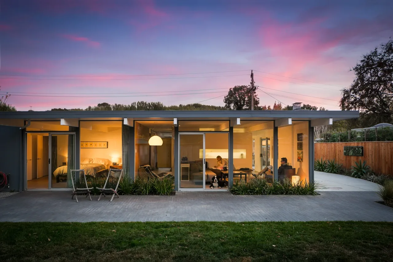Appleberry Drive Residence features floor-to-ceiling glazing and a flat roof with landscaped front yard and gravel driveway.