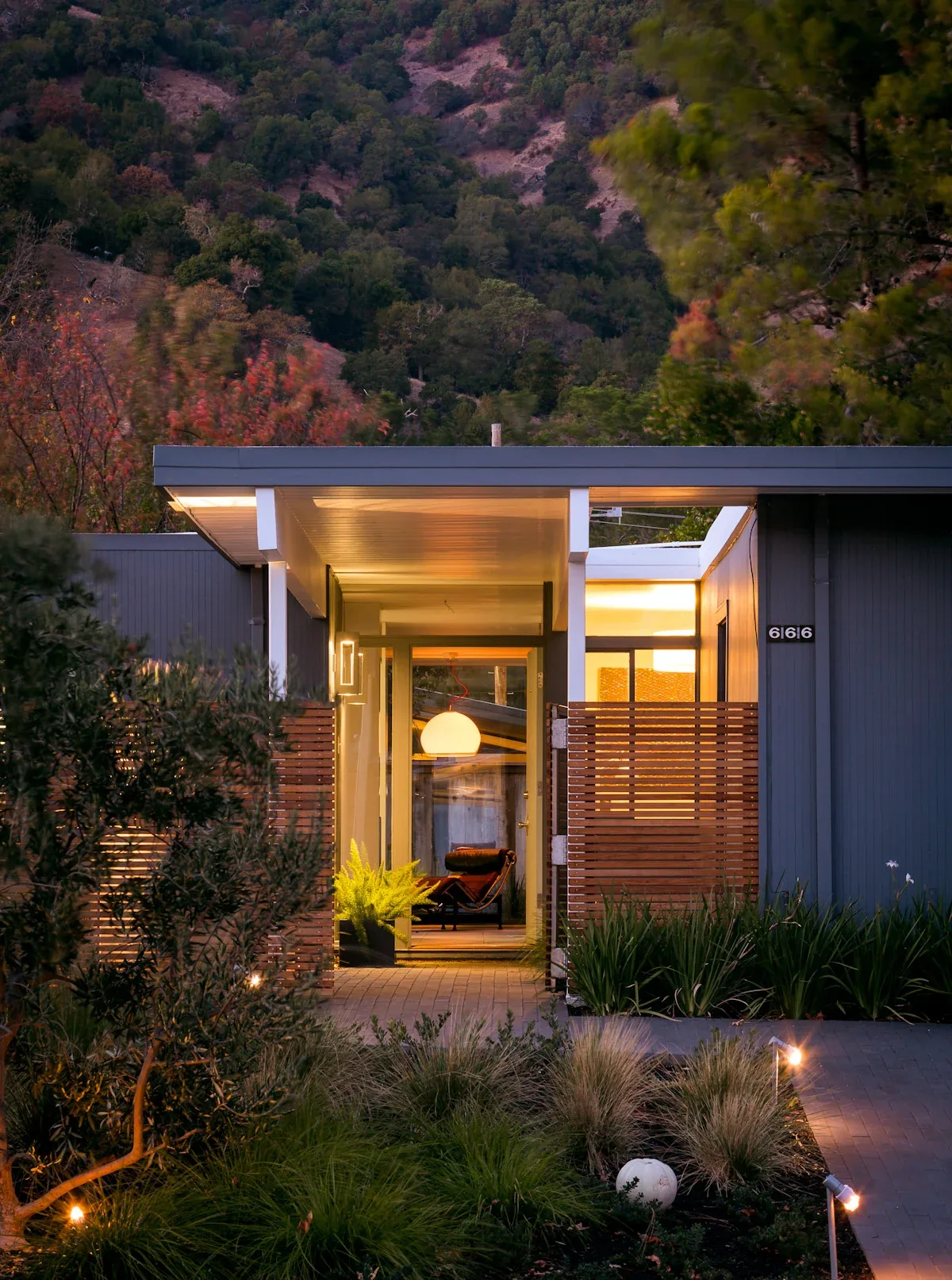The Appleberry Drive residence features a modern entryway with floor-to-ceiling glass doors framed by wood slat fencing and ambient exterior lighting.