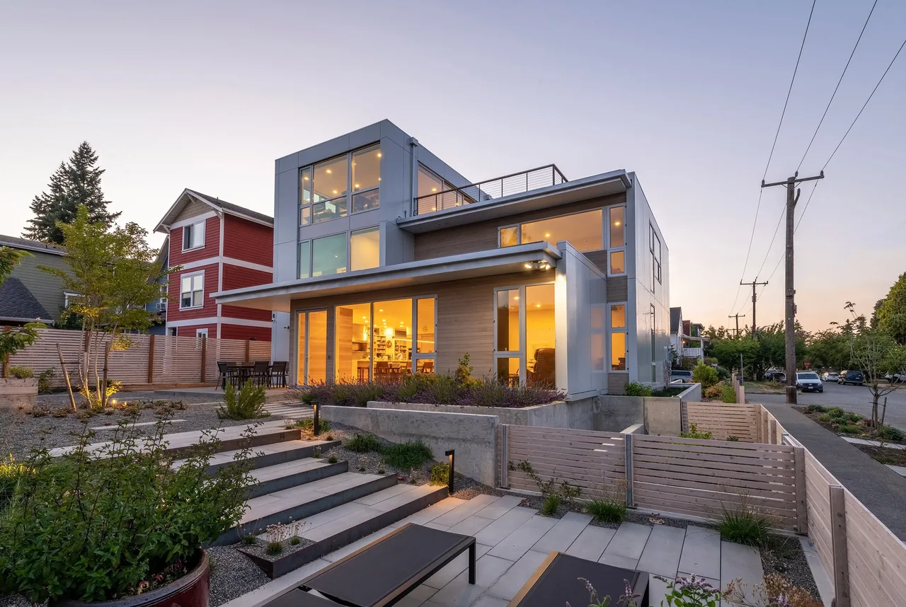 Exterior rear view of the Greenwood Residence showing a modern design with large windows and open outdoor landscaping at dusk.