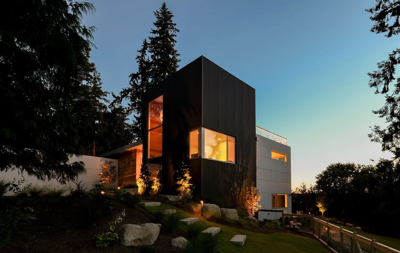 Sammamish Residence features black metal siding and vertical windows, set on a landscaped hillside with concrete stairs and boulders.