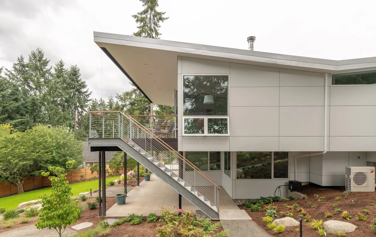 The Sammamish Residence features metal siding, an angled roof, and concrete stairs leading to a raised outdoor living area.