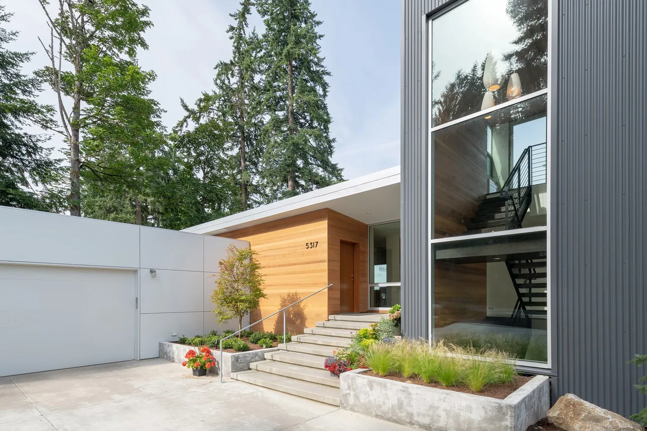 The Sammamish Residence features concrete stairs leading to a wood-clad entry with adjacent metal siding and tall windows.