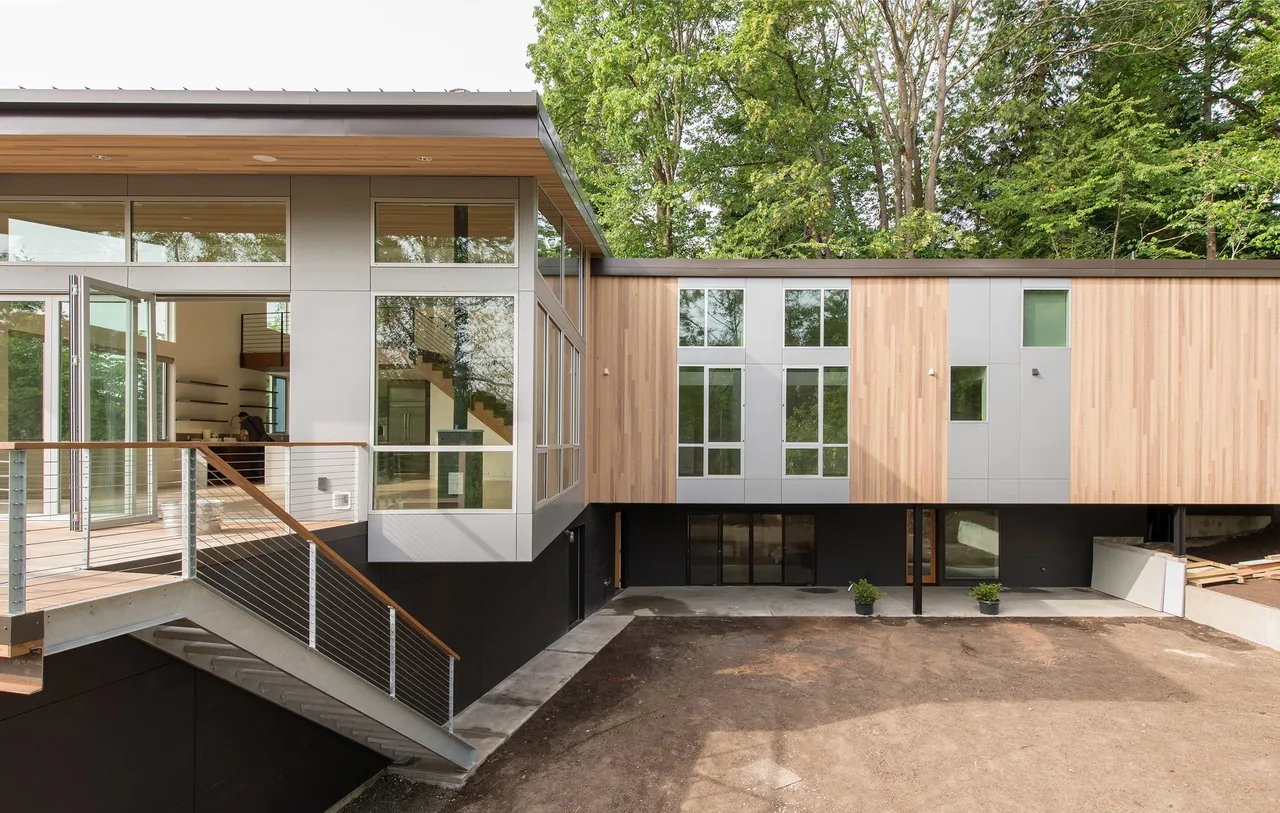 Mercer Island Residence features a modern design with floor-to-ceiling glazing, wood siding, and an open stair leading to a patio deck.