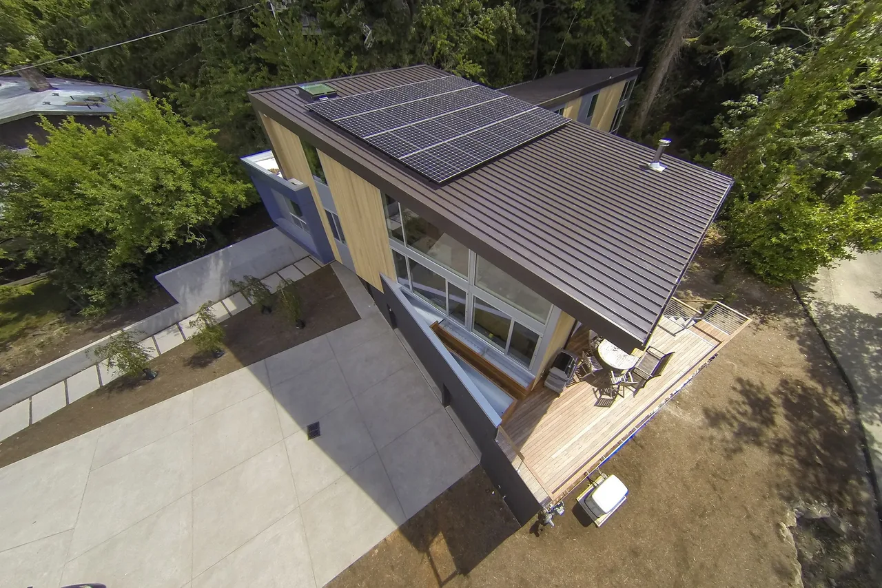 Mercer Island Residence features a standing seam metal roof with solar panels and an elevated wood-clad exterior deck.