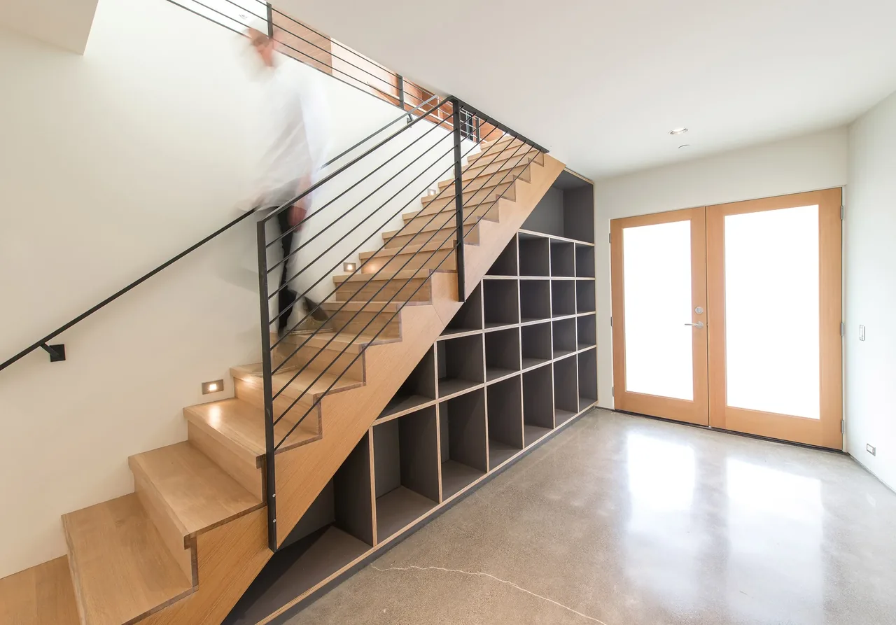 The Mercer Island Residence entryway shows wood stairs with black metal railings and built-in cubby storage below.