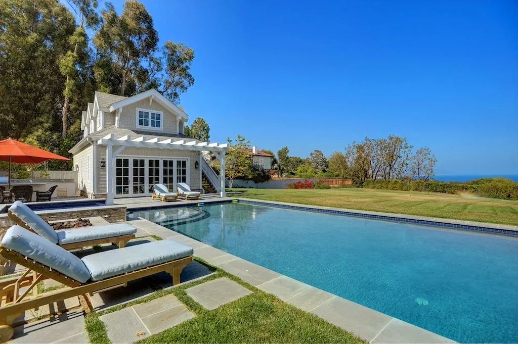 The Dume Drive Traditional project features a pool house with a pergola next to a swimming pool and lawn.