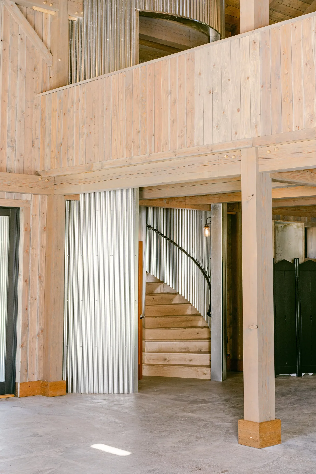 Interior features light wood staircase next to corrugated metal panel wall in a spacious room with exposed wood structure.