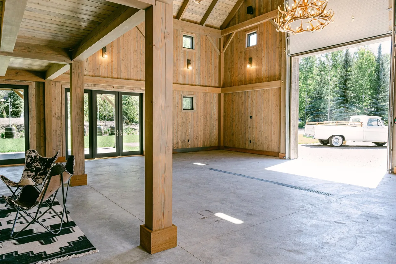 Garage interior with weathered wood siding, exposed beams, multiple windows, and a large open garage door showing a white pickup outside.