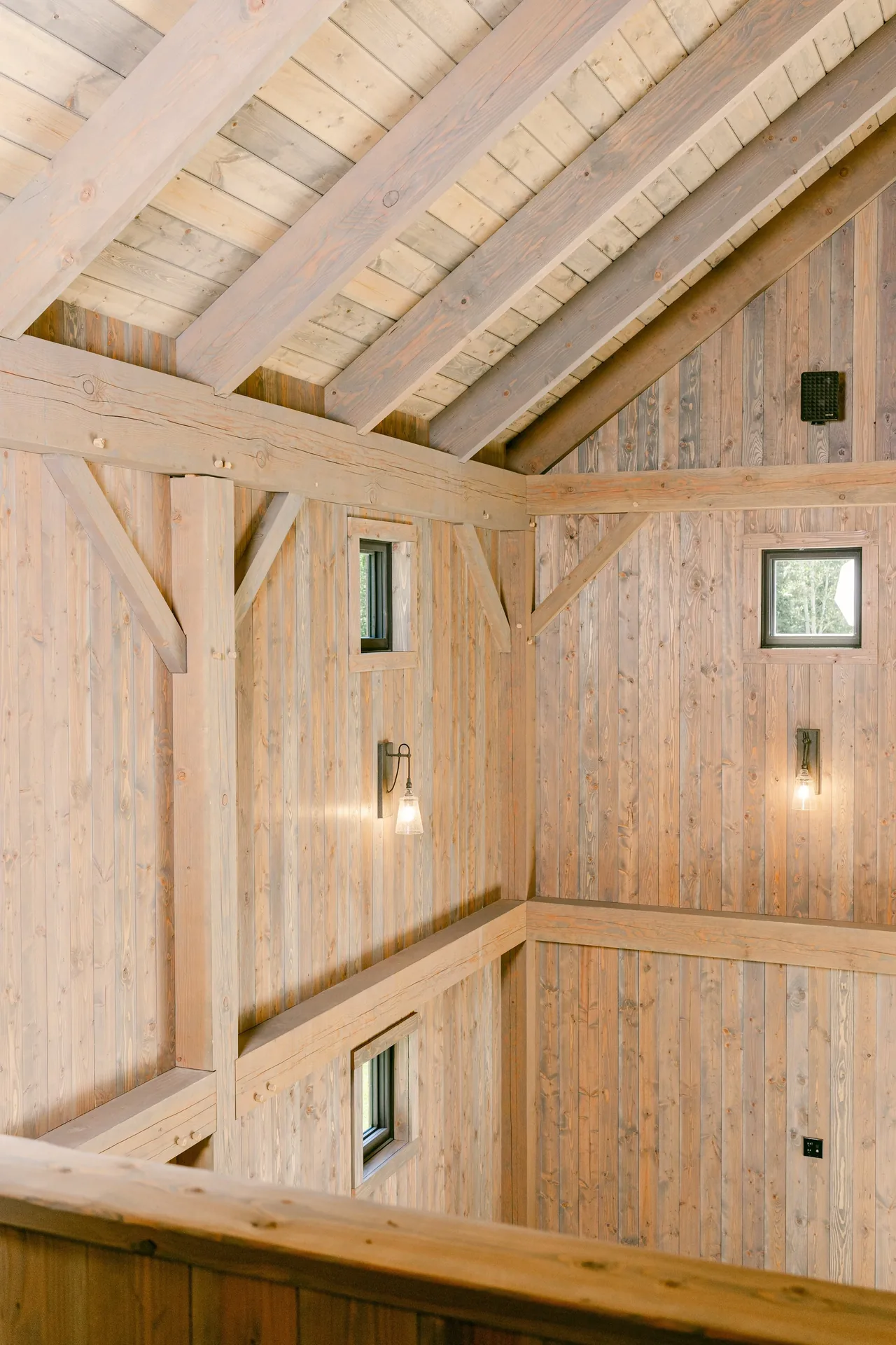 The Riverside Retreat interior features exposed wood beams and vertical wood siding with wall-mounted light fixtures.
