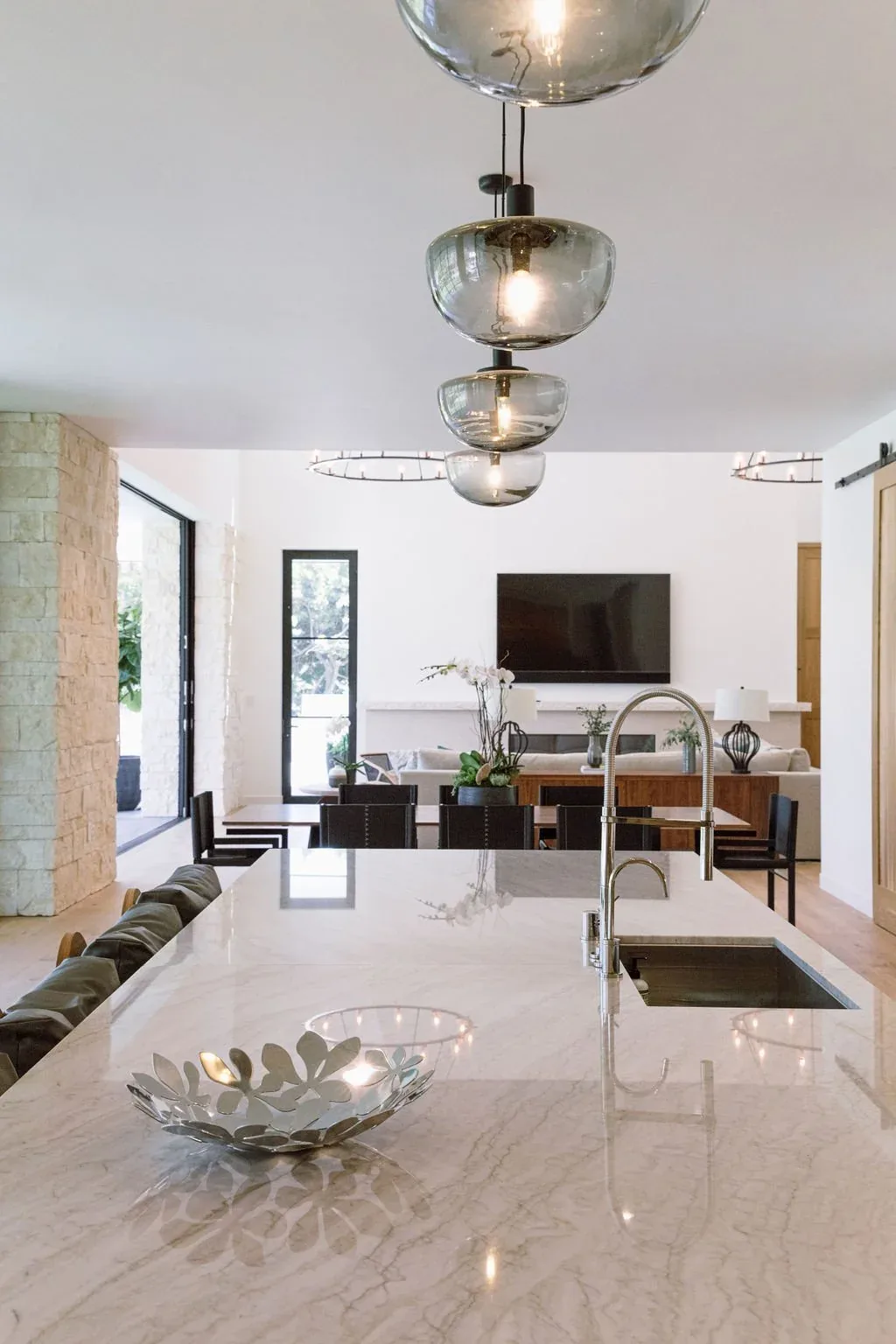 Marble kitchen island with stainless steel faucet overlooks dining and living areas with black window frames.