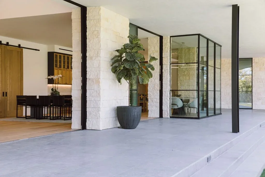 The Malibu Modern features floor-to-ceiling glazing and stone exterior columns opening to a spacious patio and dining area.
