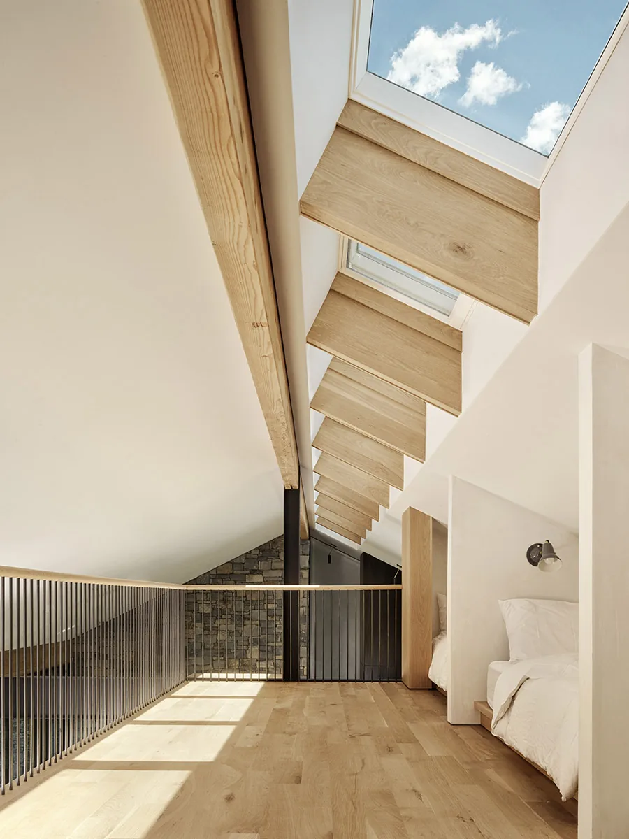 Loft bedroom detail features wood flooring, angled skylights with wood trim, and metal railings overlooking a lower level with stone wall.