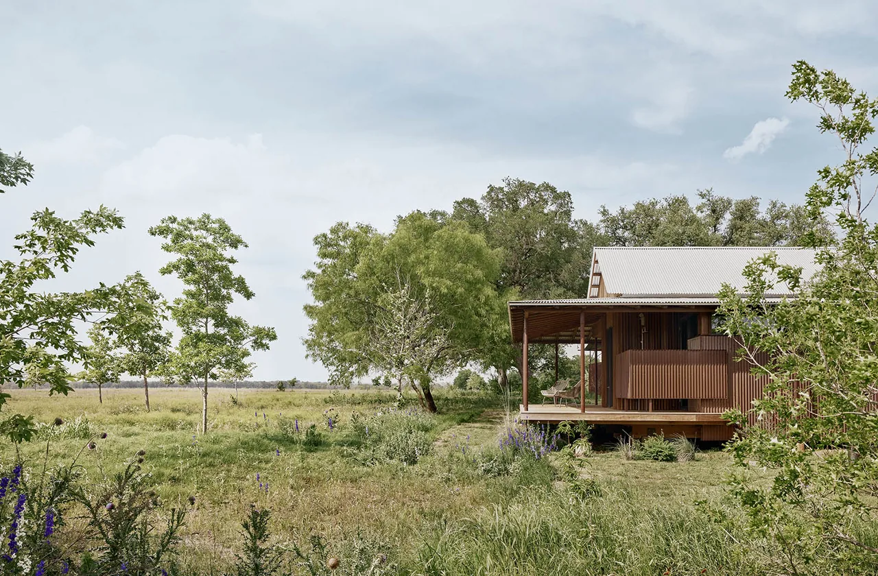 Roam Ranch features a raised ranch-style house with a metal roof and a porch surrounded by natural landscaping.