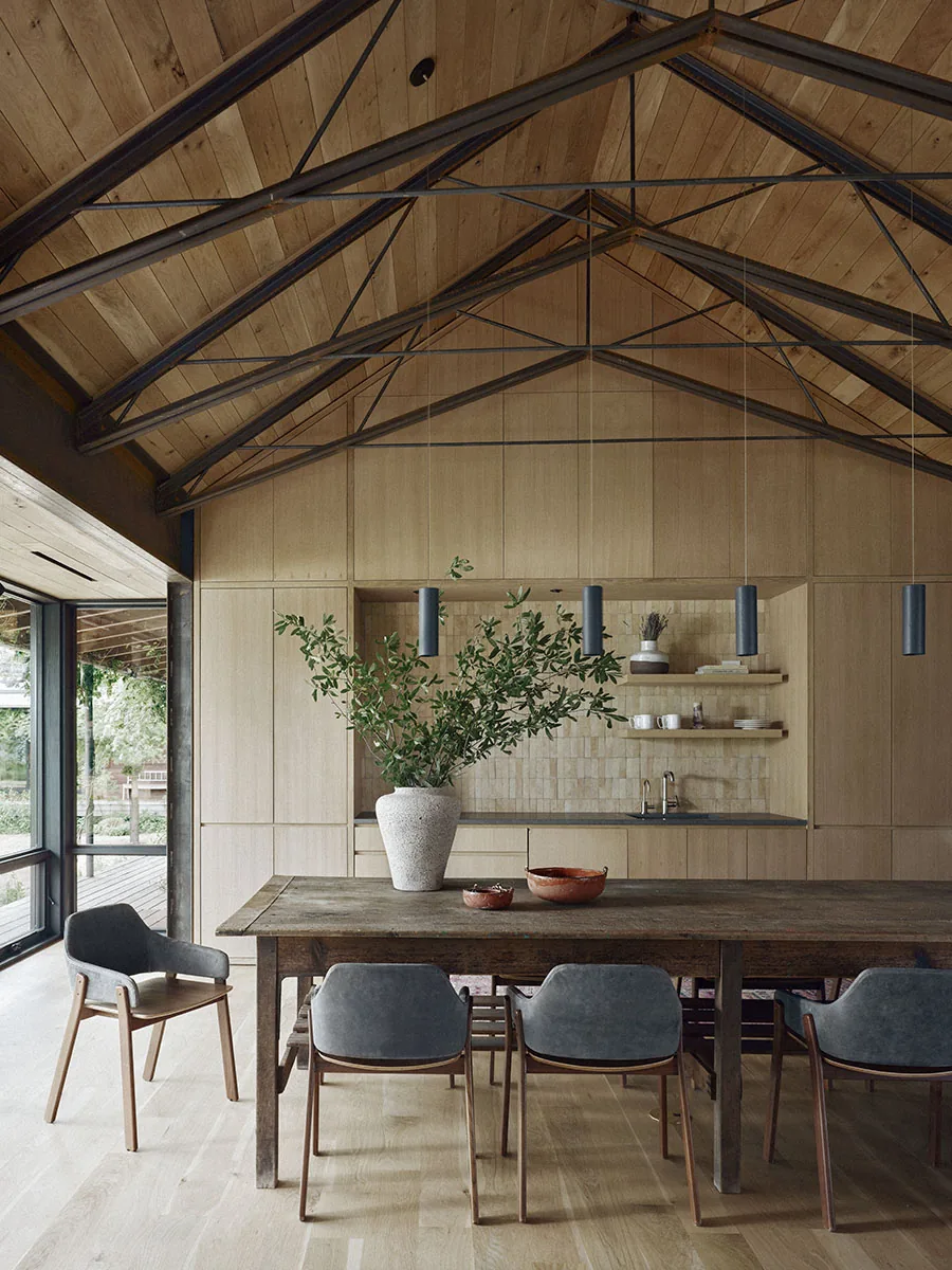 Dining space with a rustic wood table, gray chairs, pendant lights, and vaulted ceiling with exposed steel trusses at Roam Ranch.