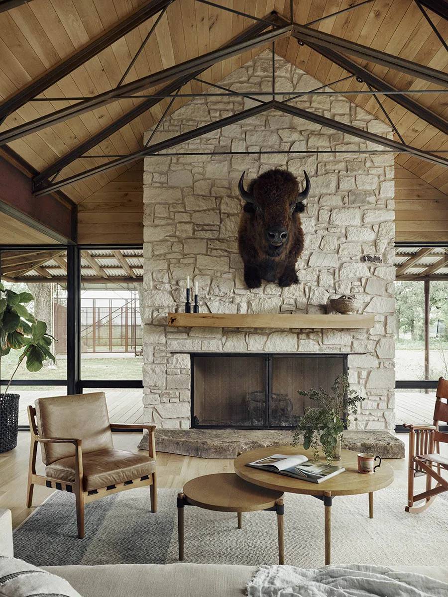 Living area features a vaulted wood ceiling and a large stone fireplace with a bison head mount in Roam Ranch project.
