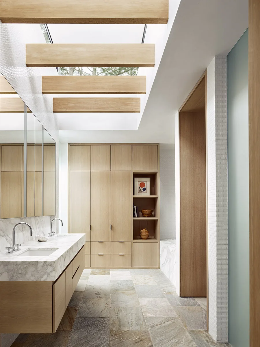 Bathroom features marble countertop with dual undermount sinks, wood cabinetry, stone floor tiles, and horizontal wood ceiling beams.