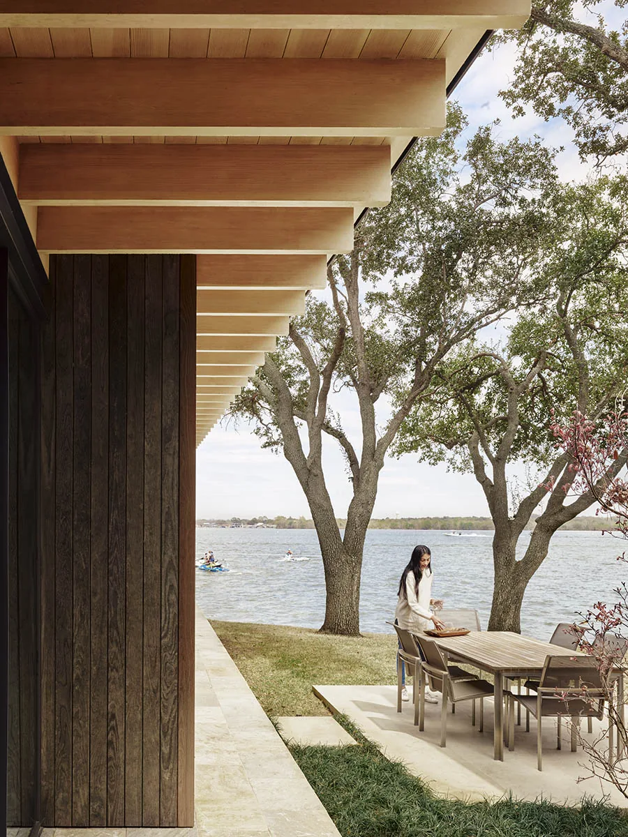 Lakefront patio with wood dining set and prominent exposed wooden roof beams overhang provides shaded outdoor living space.