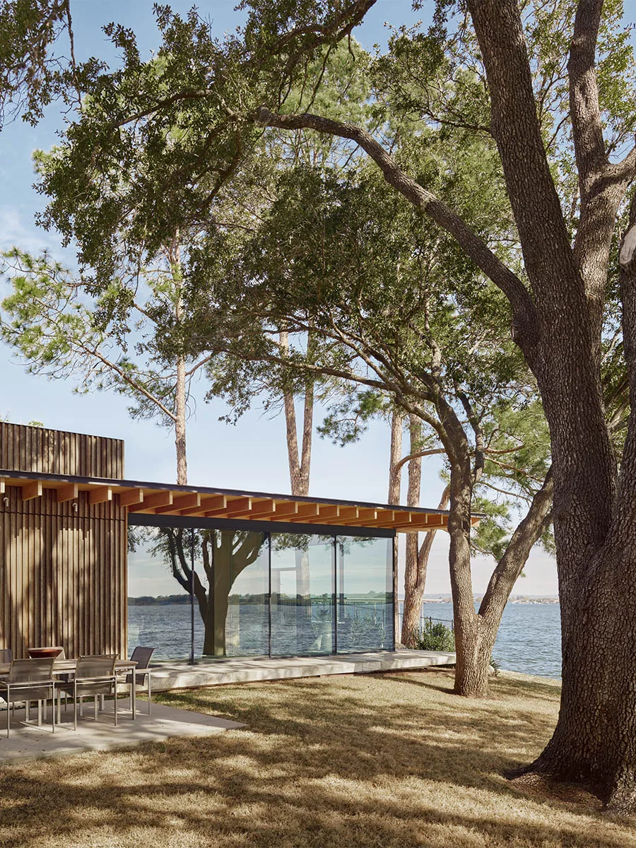 Lake Retreat + Boathouse features floor-to-ceiling glazing and wood siding overlooking a lake.