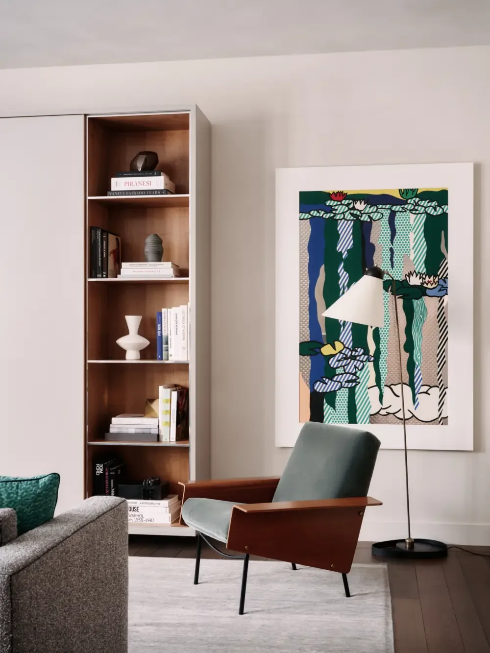 Modern living room corner featuring a wood frame armchair, built-in wood accent bookshelf, and colorful abstract artwork on a neutral wall.