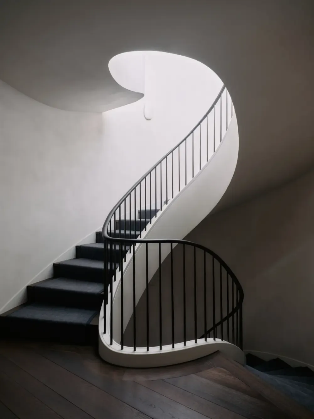 The Presidio Heights Residence features a sculptural curved staircase with black metal railings and an overhead light well.