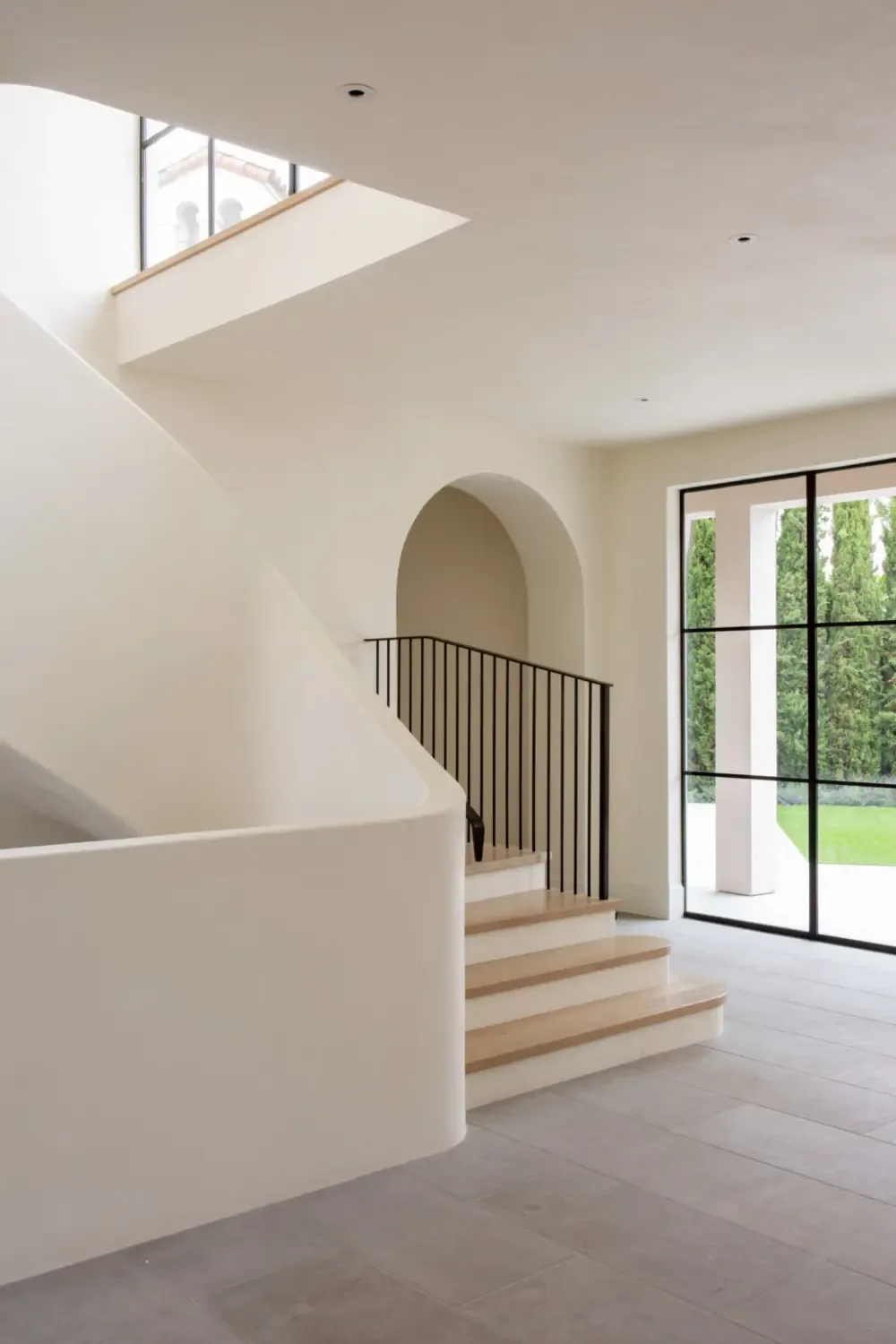 Stairwell area with curved wall, arched doorway, and floor-to-ceiling black-framed window in a neutral-toned interior.