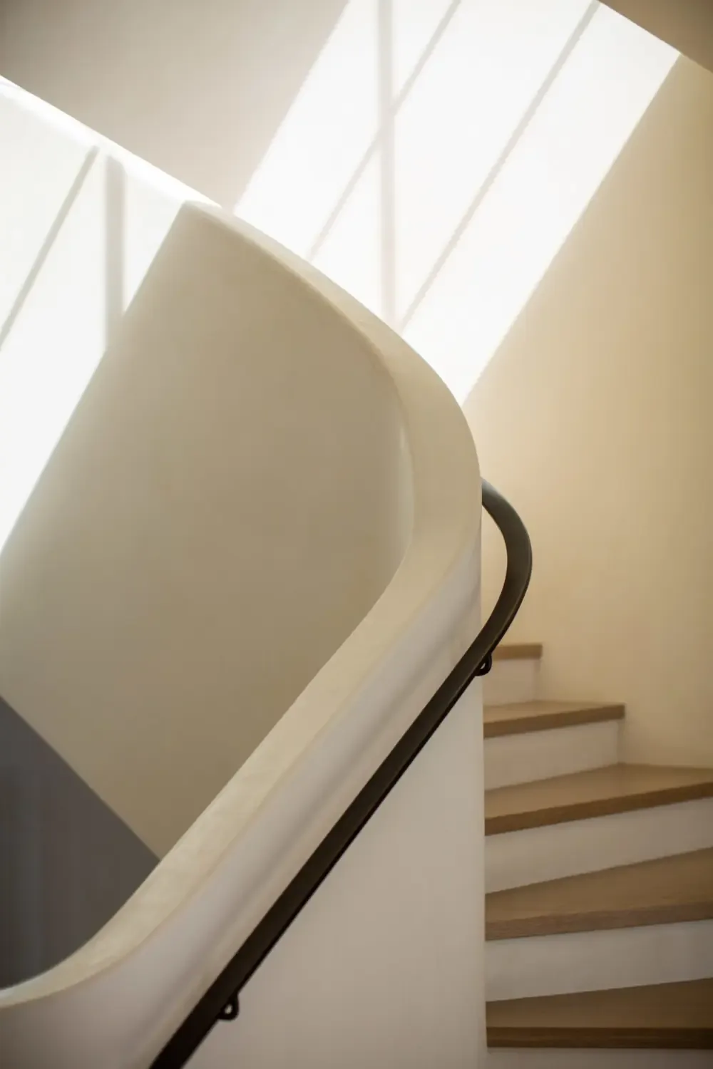 The Sea Cliff Sculptural home features a curved plaster stair wall paired with a sleek black handrail accentuated by natural light.