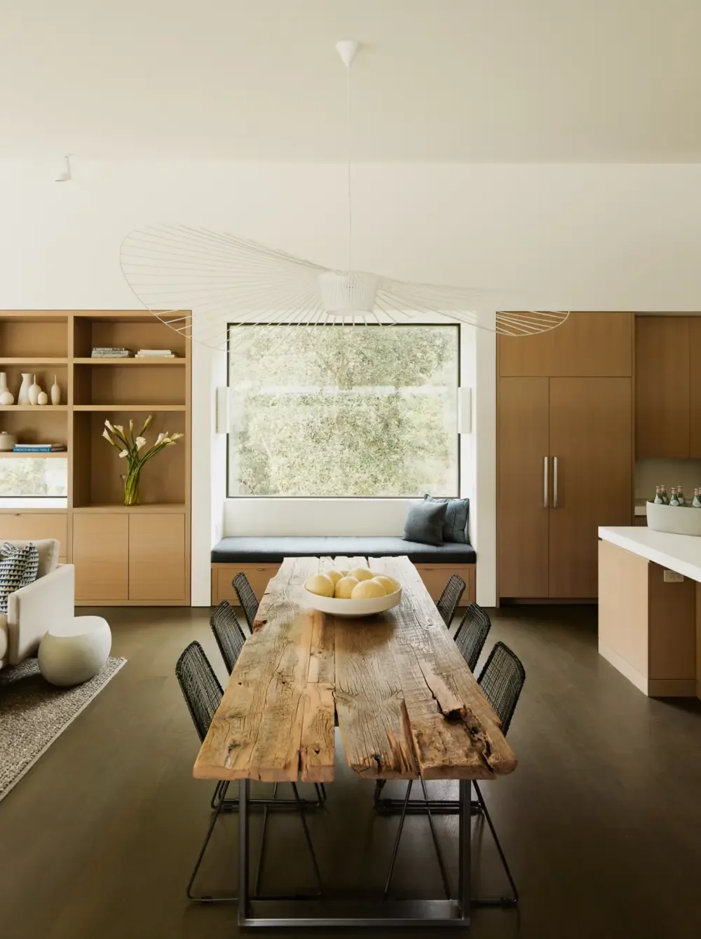 Dining area features a rustic wood table with black wire chairs and built-in wood cabinetry around a window seat with cushions.