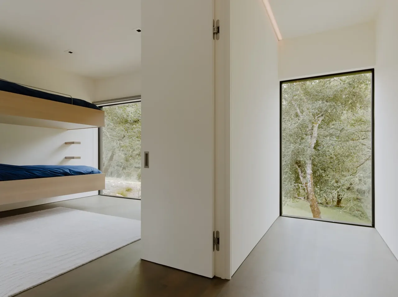 Bedroom with floating wooden bunk beds and large corner windows overlooking natural landscape.