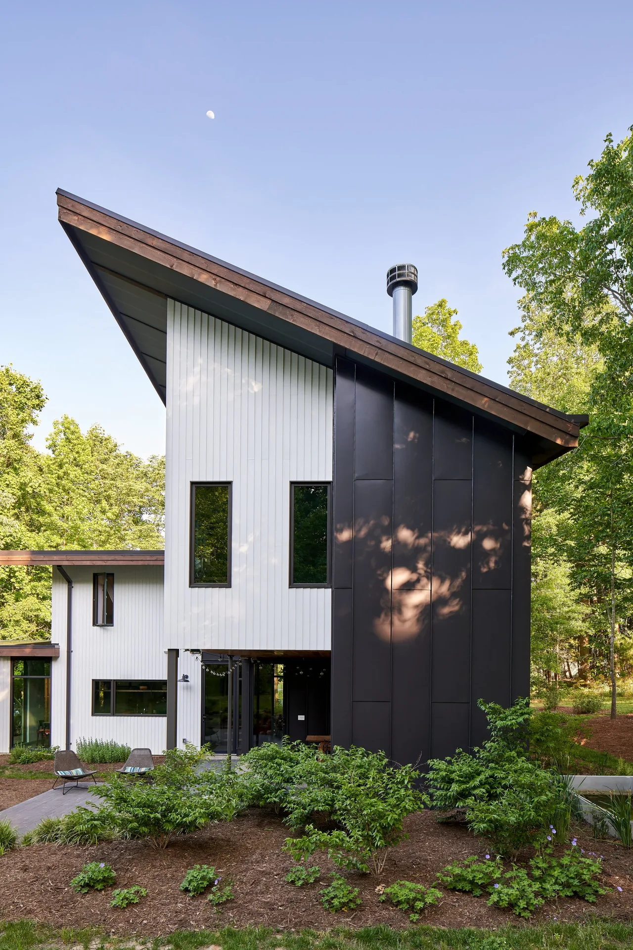 Modern home featuring vertical siding in black and white with a steep sloped roof and metal chimney vent.
