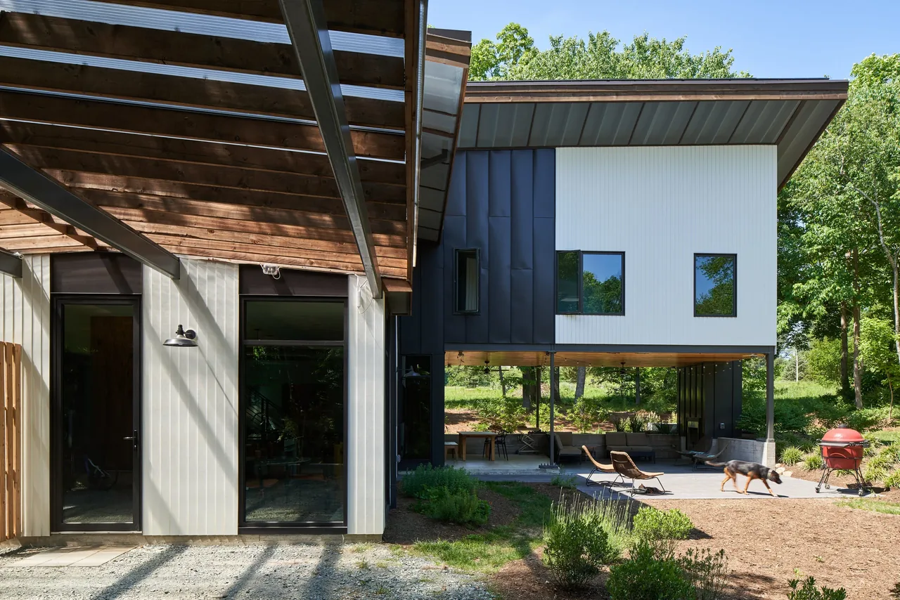 Modern two-story home with vertical wood siding, black framed windows, and an open covered patio in a wooded landscape.