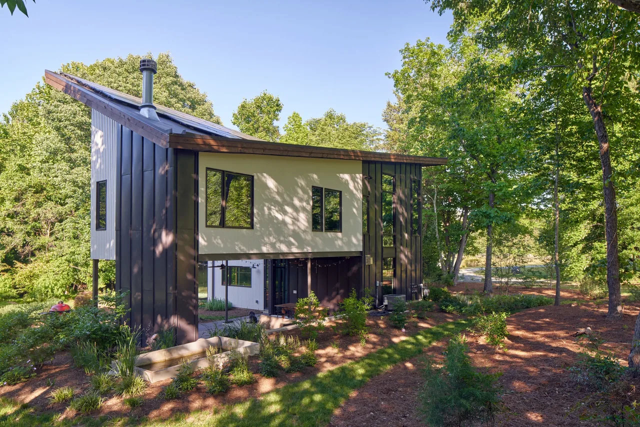 Acorn Acres features a two-story modern home with vertical siding and a sloped roof on a wooded site.