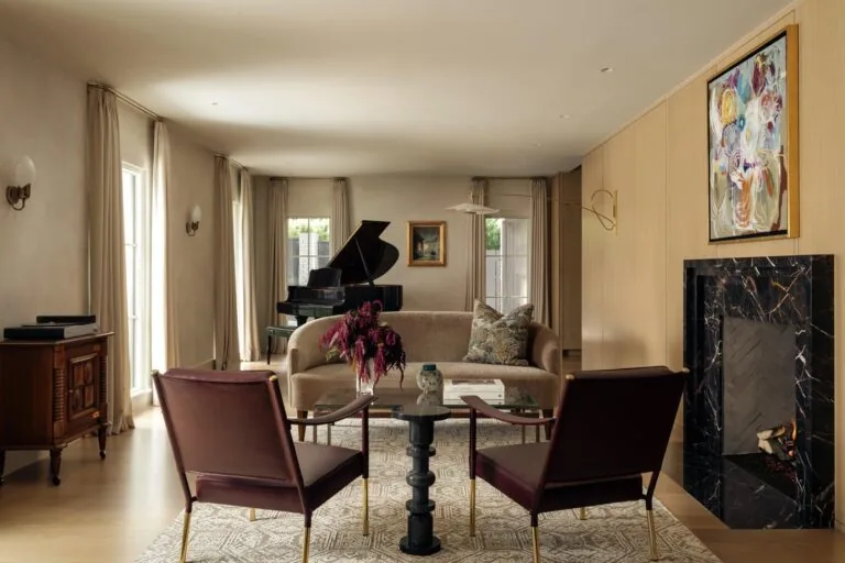 Living room featuring a black marble fireplace, leather chairs, beige sofa, and grand piano with natural light from tall windows.