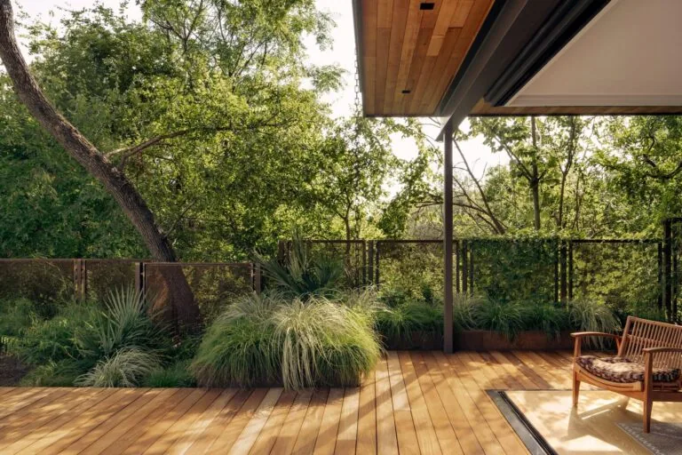 Outdoor wooden deck featuring terraced landscaping and a metal railing with greenery in a natural setting.