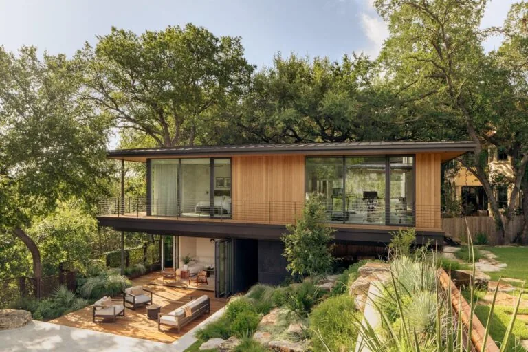 The Old Enfield project features a raised modern house with floor-to-ceiling windows and wood siding integrating into a wooded landscape.