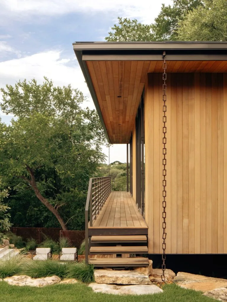 This residence at Old Enfield features horizontal wood siding and a raised balcony with metal railing overlooking terraced landscaping.