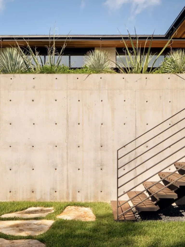 Concrete retaining wall with outdoor metal and wood stairs leading to an upper patio above a landscaped yard.