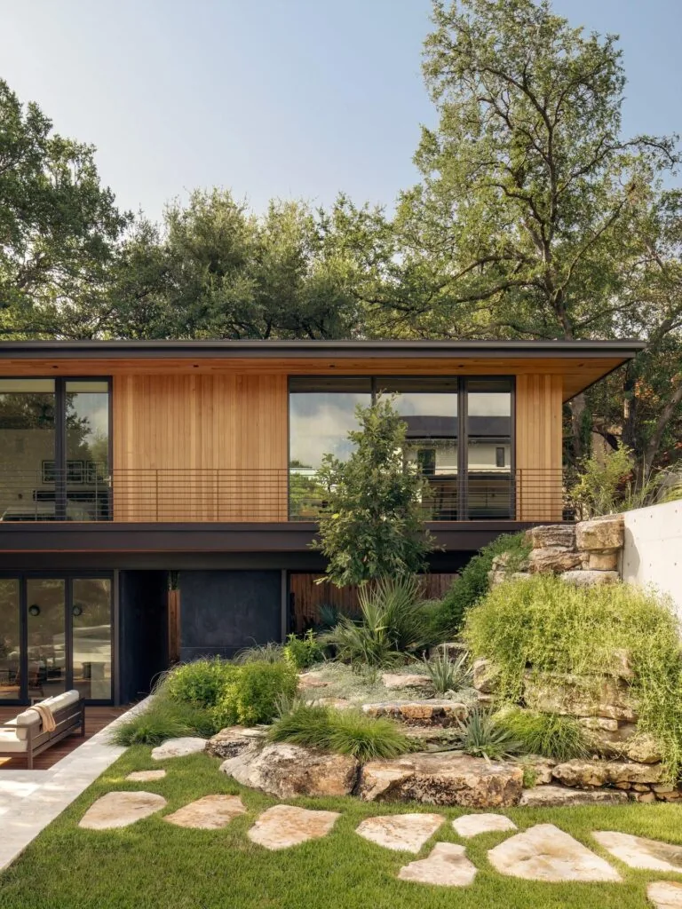 The Old Enfield house features wood siding above and large glass sliding doors below, set against a landscaped rock garden.