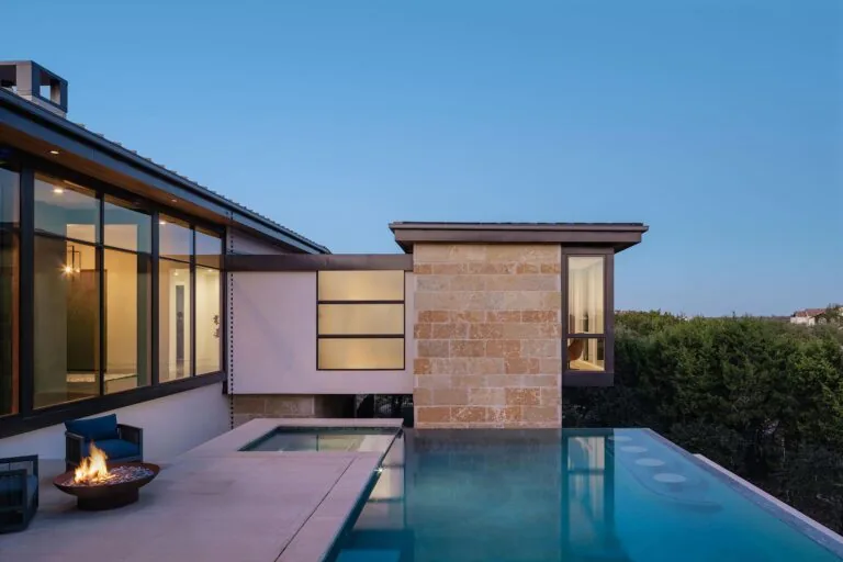 Infinity pool with built-in seating and fire pit beside a modern house at twilight in Laceback Terrace project.