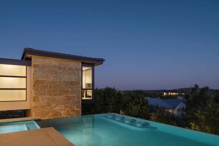 Laceback Terrace features an infinity pool with built-in seating against a stone chimney wall, captured at dusk.